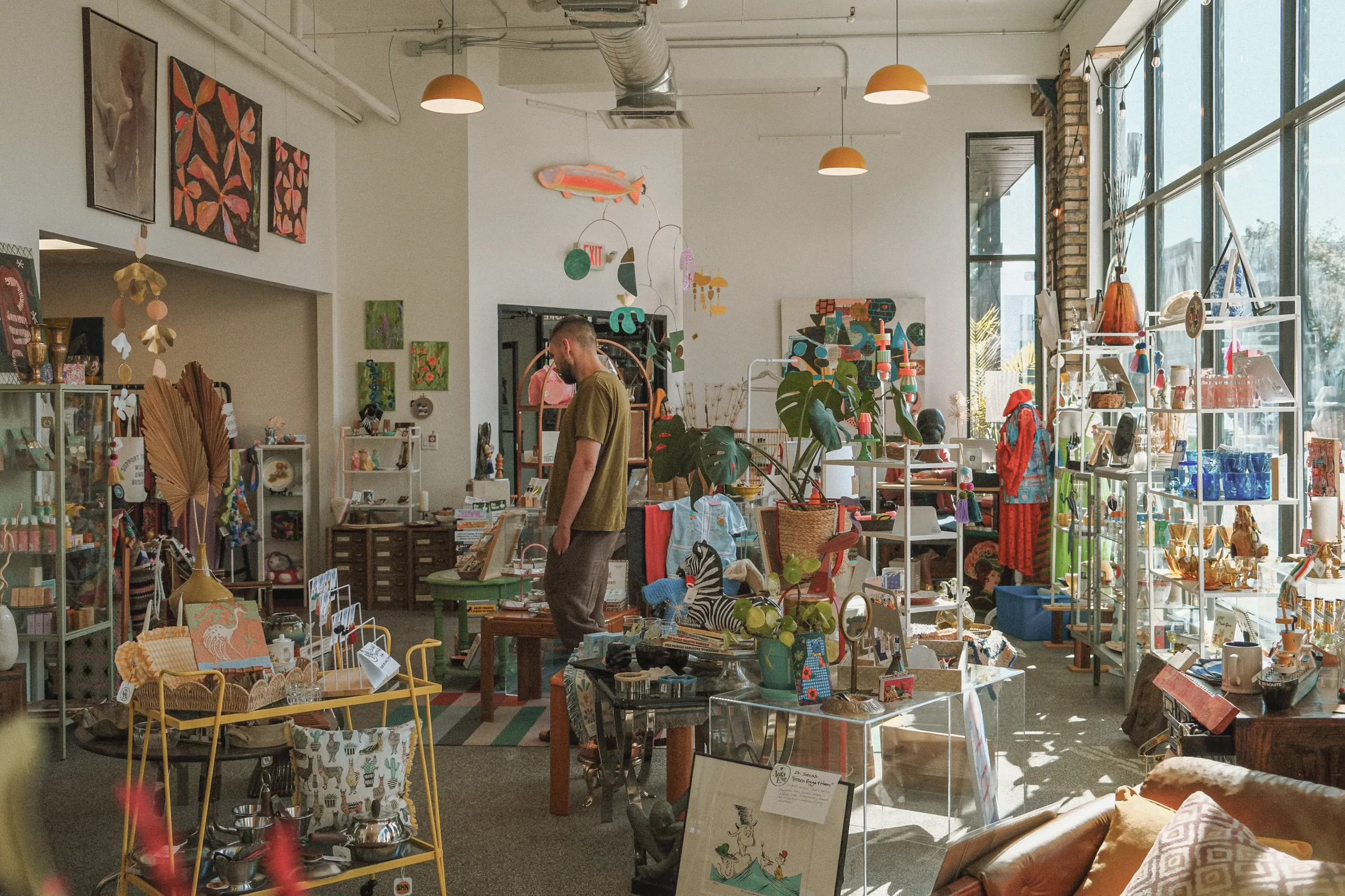 Interior of Aura Eye pop-up shop in Duluth, featuring vintage and artisan goods, colorful decor, a man browsing items, and various whimsical products displayed on shelves and tables.